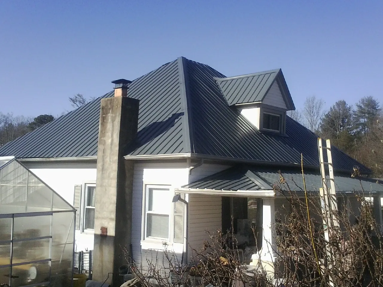 Dark blue standing seam metal roof on a white farmhouse with dormer — Slate & Tile Roof Repair by Roofing Brothers in Maitland