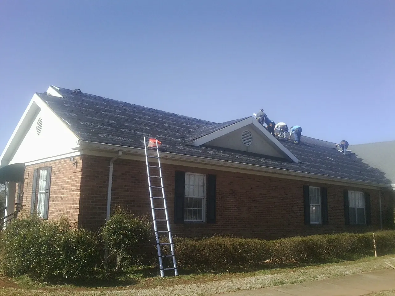 Crew tearing shingles off a brick ranch roof with a ladder set — Metal Roof Repair work by our crew in Maitland